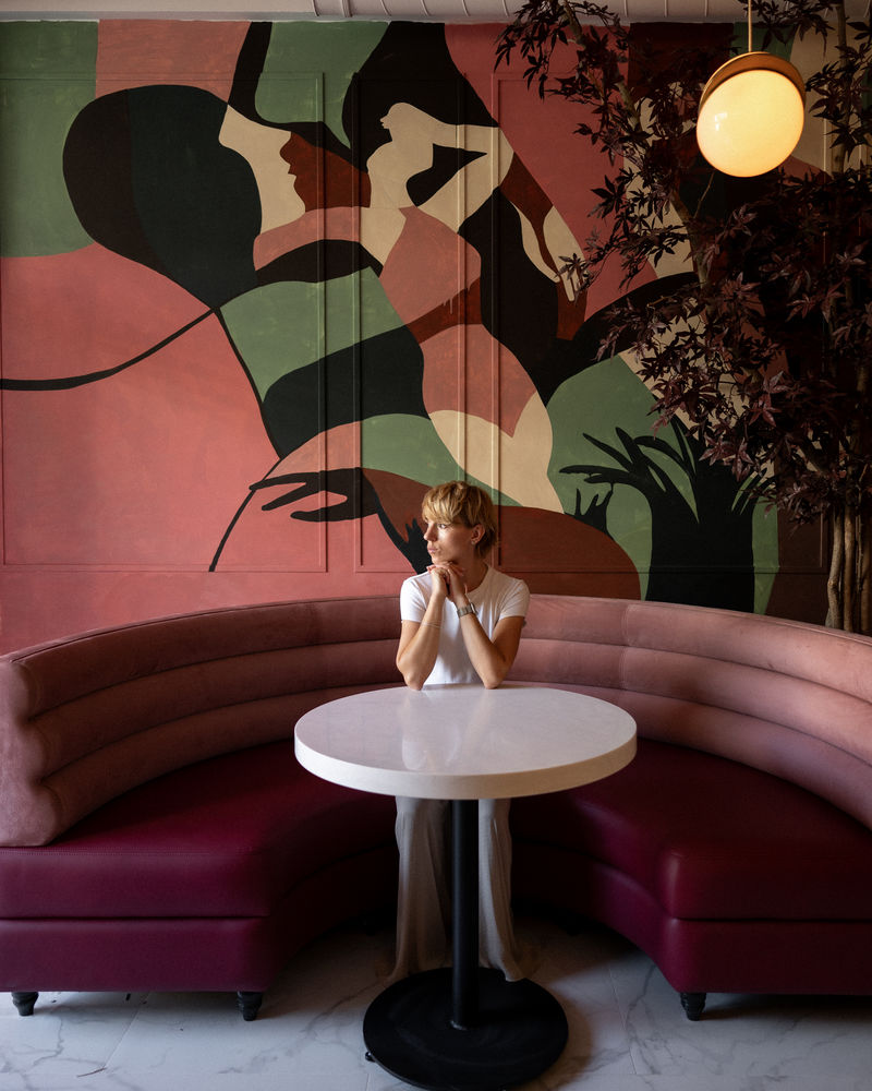 Al Bocconcino mural — Elena Kachanova at pink sofa with The Dawn mural